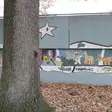 Wandmalerei von Tieren auf grauer Wand mit einem Baum im Vordergrund.