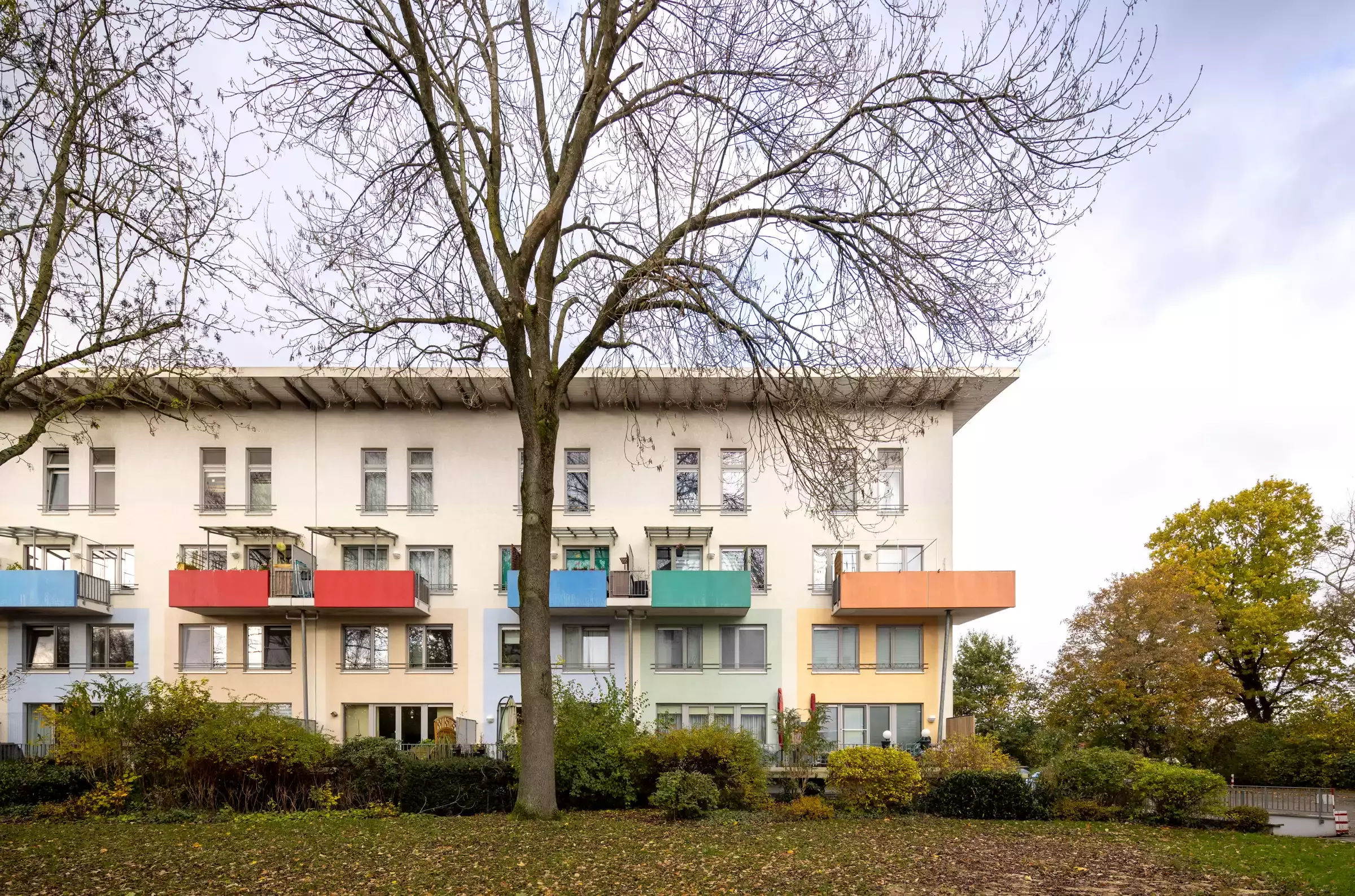 Blick auf ein weisses eckiges Mehrfamilienhaus mit bunten Balkonen