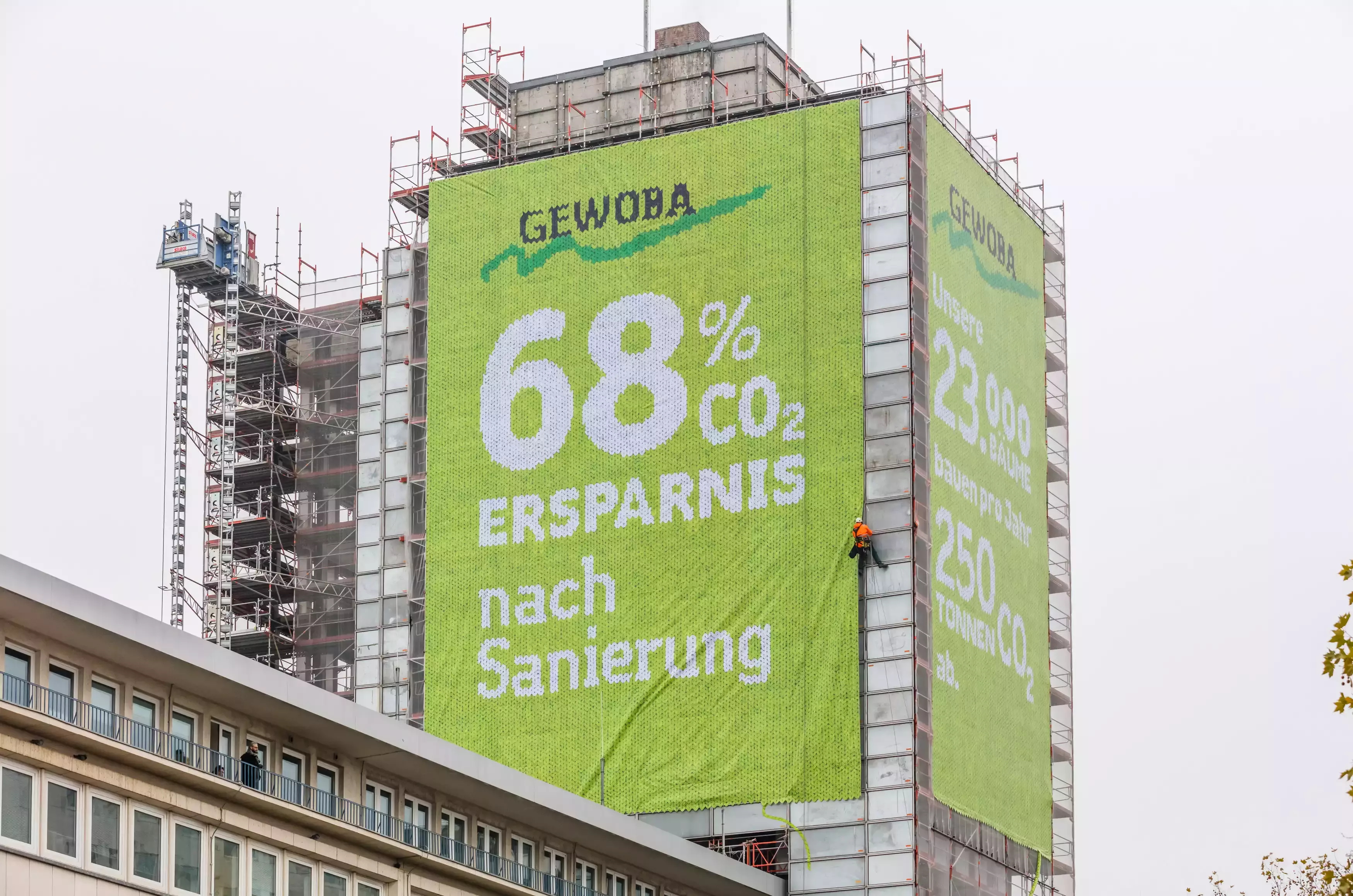 Eingerüstetes Hochhaus mit einem grünen Banner zur CO2-Ersparnis nach der Sanierung