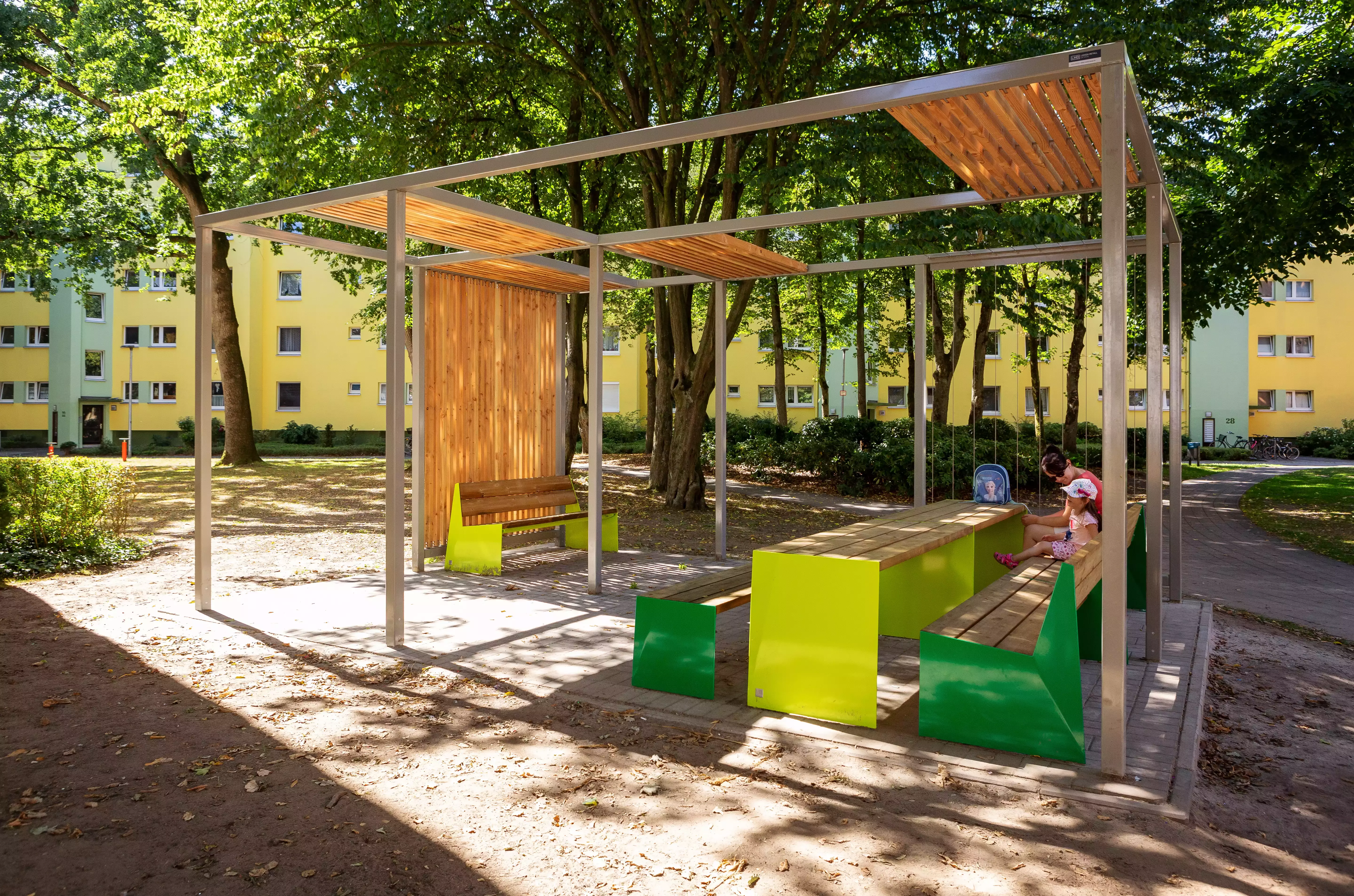 Ein offener Pavillon mit bunten Tischen und Bänken unter Bäumen