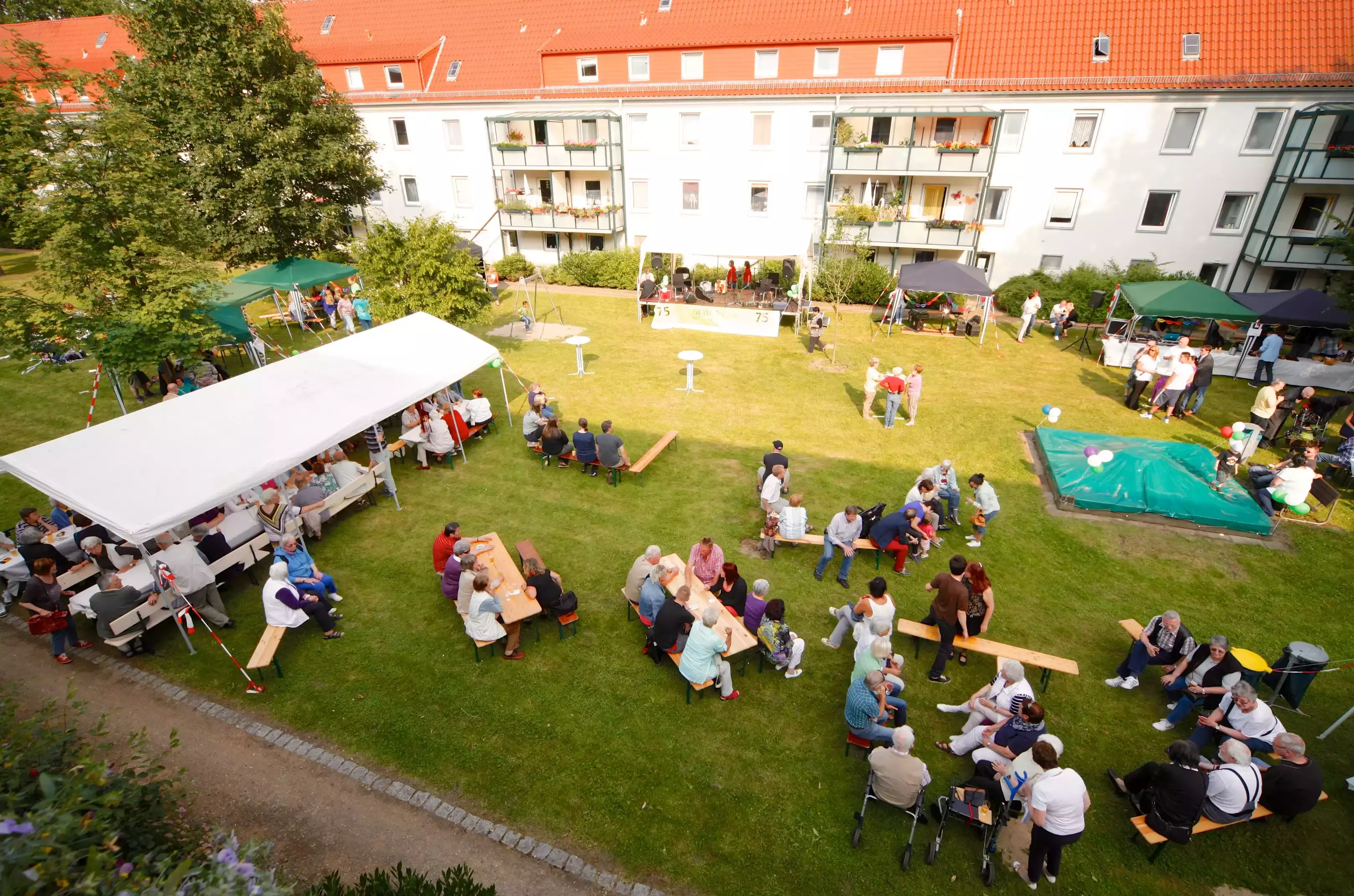 Menschen auf Bierbänken bei einem sonnigen Gartenfest hinter einem Wohnblock